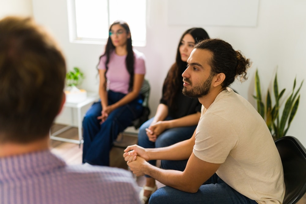 Thérapie de groupe pour jeunes adultes : Soutien et écoute Groupe de soutien de jeunes adultes écoutant attentivement lors d'une séance de thérapie en cercle.